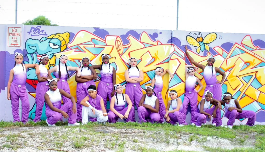 BeatStreet Baddeez competitive dance team in purple costumes posing in front of a colorful graffiti mural