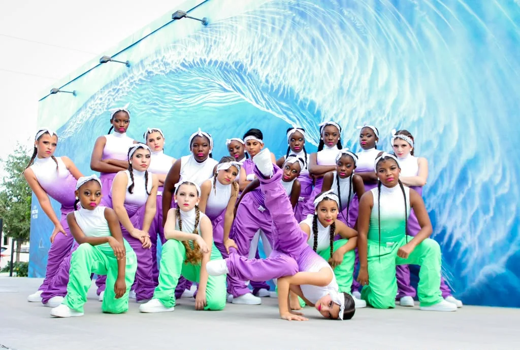 BeatStreet Baddeez dancers in purple and green costumes posing in front of a wave mural